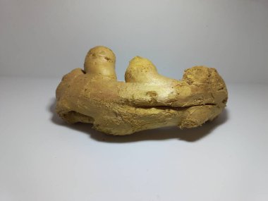 Beyaz yüzeyde taze zencefil kökü. Tarafsız bir arkaplanı olan beyaz bir yüzeye yerleştirilmiş taze zencefilli rhizomu yakından çek. Zencefil kökü pürüzlü, bronzlaşmış bir ten ve düzensiz, doğal dokusunu ön plana çıkaran bir şekil içerir..