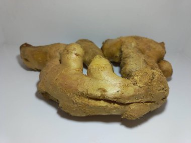 Beyaz yüzeyde taze zencefil kökü. Temiz beyaz bir zemin üzerine yerleştirilmiş temiz, beyaz bir zencefil köküne yakın plan. Zencefil, organik özelliklerini sergileyen, topuzlu çıkıntılar ve doğal düzensizliklerle bronzlaşmış sert bir cilde sahip.