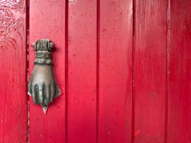 Ege ve Akdeniz mimarisinin tipik bir örneği olan el şeklinde metal kapı tokmağı olan kırmızı ahşap kapıya yakın plan..