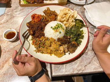 Endonezya 'nın çeşitli pişirme yöntemleriyle pişirilmiş domuz etiyle çevrili beyaz pirinç. Lezzetli, lezzetli ve renkli domuz eti ve sebze kızartması, siyah bir kasede beyaz pirinç yatağının üzerinde..