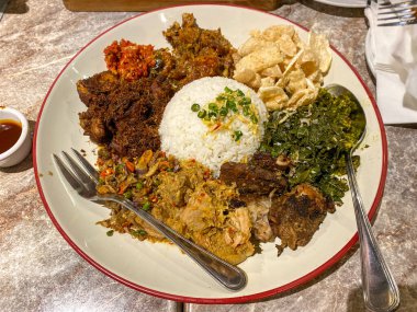 Endonezya 'nın çeşitli pişirme yöntemleriyle pişirilmiş domuz etiyle çevrili beyaz pirinç. Lezzetli, lezzetli ve renkli domuz eti ve sebze kızartması, siyah bir kasede beyaz pirinç yatağının üzerinde..