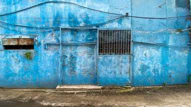 Mavi duvarda eski ve kirli, mavi, çelik, katlanmış bir kapı.