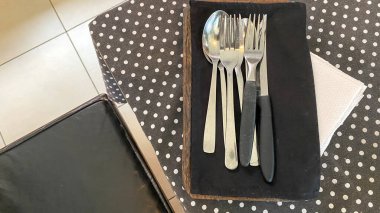 Tahta masadaki siyah peçeteye kaşık, çatal ve bıçak. Siyah masada beyaz noktalı Cutleriy.