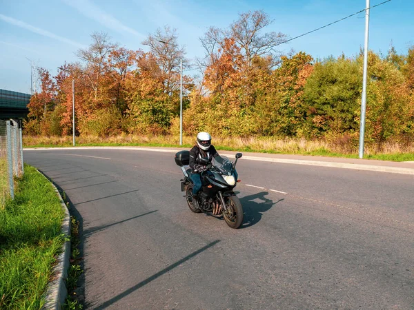 Pengendara sepeda motor bergerak. Pengendara sepeda motor perempuan mengendarai motor hitam lalu lintas di jalan pedesaan musim gugur — Stok Foto