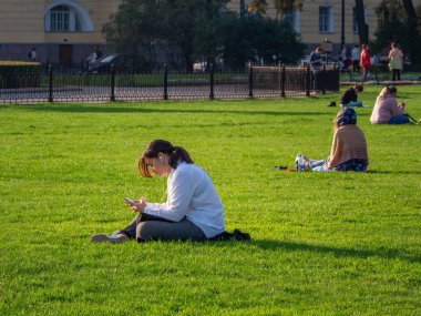 30 Eylül 2020, Saint Petersburg, Rusya. Bir öğrenci yeşil çimenlikte bir sesli kitap dinler..