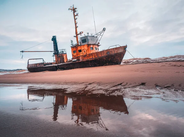 An old rusty fishing boat washed up on a sandy beach in the Barents Sea. Authentic the North sea. Teriberka.