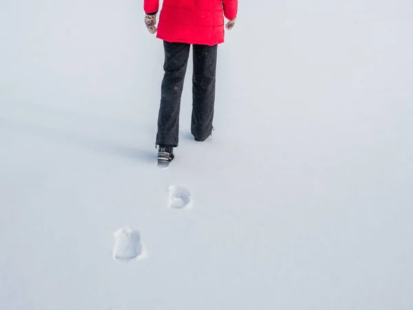 穿着红色夹克的女人在雪地上行走 脚印在雪地后面 — 图库照片