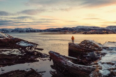 Graveyard of ships, winter sunset view in an old fishing village on the shore of the Barents sea, the Kola Peninsula, Teriberka, Russia. clipart