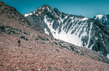 Aşırı eğlence ve dağ turizmi. Dağ yolunda bir erkek yürüyüşçü. Arka planda, karla kaplı büyük dağlar. Boşluğu kopyala.