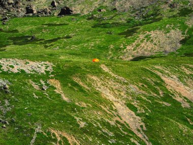Küçük bir çadırı olan yeşil bir dağ yamacının minimalist manzarası. Yeşil tepelerde kayaların arasında çadırı olan manzaralı dağlık bir arazi..