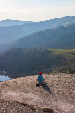 Dağlarda yoga, doğada rahatlama. Atletik ince kız gün batımında bir kayanın üzerinde lotus pozisyonunda meditasyon yaparken oturur. Dikey görünüm.