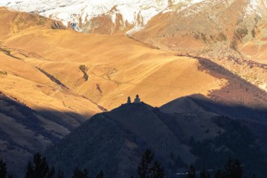 Gün batımında Gergeti Üçlemeci Kilisesi 'nin altın rengi. Uzaktan bak. Kazbek Dağı 'nın sonbahar manzarası, Stepantsminda, Georgia. Georgia 'nın doğası.. 