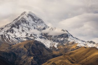 Sonbahar renklerinde olağandışı kayaları olan çok renkli dağ manzarası. Soyu tükenmiş bir stratovolcano olan Kazbek Dağı, Rusya ile Gürcistan arasındaki sınırda yer almaktadır. Boşluğu kopyala.