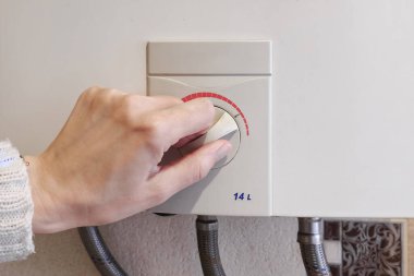 Hands adult women set the temperature of the water in the gas boiler. Close up. 