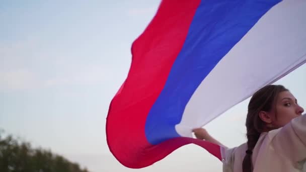 Het symbool van Rusland is een driekleurige vlag: wit, blauw en rood. Een jonge vrouw houdt een vlag achter haar rug in de wind — Stockvideo