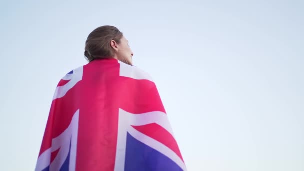 Brittiläinen nainen seisoo lippu selässään ja katsoo kaukaisuuteen. Brittiläinen itsenäisyys, naispuolinen patriootti vapaassa maassa — kuvapankkivideo