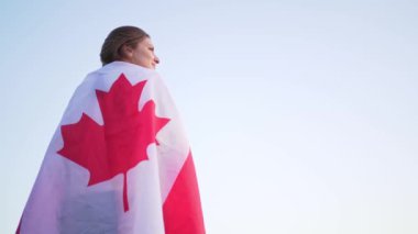 Omzunda bayrak olan bir insan gururla uzaklara bakar. Arka planda hava açık. Kanada bayrağı