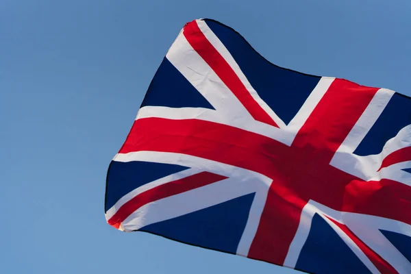 La bandera de Gran Bretaña se desarrolla en el viento al atardecer contra el cielo. Símbolo nacional de Inglaterra —  Fotos de Stock