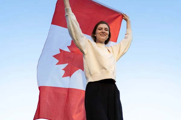 Μια όμορφη νεαρή γυναίκα με τη σημαία του Καναδά πηγαίνει στο φόντο του δάσους. Καναδός πατριώτης χαμογελάει και κοιτάζει στην κάμερα — Φωτογραφία Αρχείου