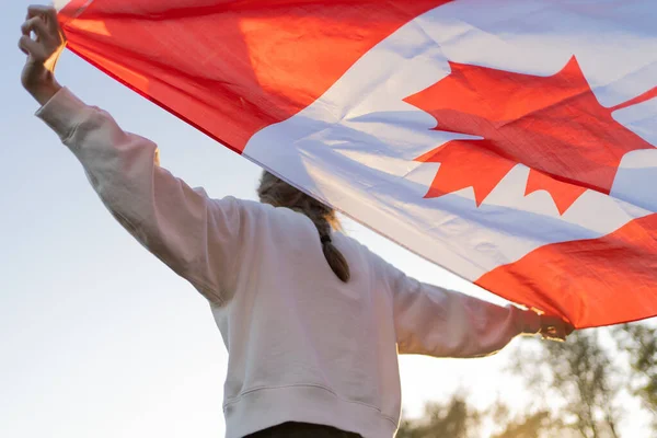 De vlag van Canada in de handen van een persoon. Canadees symbool tegen de achtergrond van een prachtige zonsondergang. Trots en onafhankelijkheid — Stockfoto