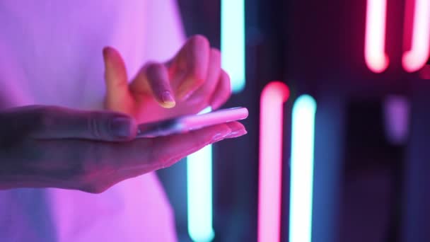 Cellulare alla luce del neon nelle mani delle donne. Una persona scrive un messaggio in una chat sullo sfondo colorato — Video Stock