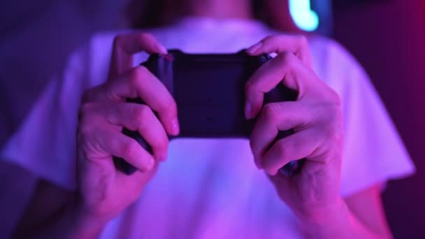 Een jonge vrouw speelt een online spel op een zwarte joystick. Neon licht in de kamer — Stockvideo