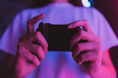 Genç bir kadın siyah bir joystick 'le online oyun oynuyor. Odanın içinde neon ışığı