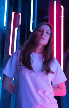 Kameraya poz veren güzel ışıklı bir bayan. Arka planda mavi ve pembe lambalar