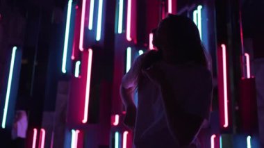 İnce kadın neon arka planda rahatça dans ediyor. Dansçının silüeti farklı renklerde güzel bir ışıkta