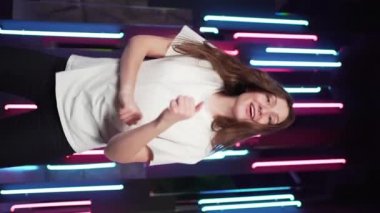 Dikey video - renkli gece ışığı, gülümseyen ve dans eden genç bayan dansçı