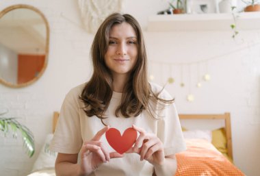 Elinde kırmızı kağıt bir kalple romantik güzel bir kadın gülümseyip kameraya bakıyor. Sevgililer Günü 'nün sembolü.