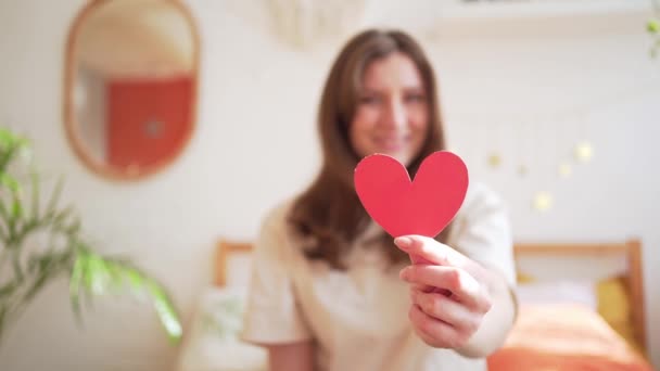 Dare amore a San Valentino. Cuore di carta rossa in mano a una giovane donna in una stanza calda — Video Stock