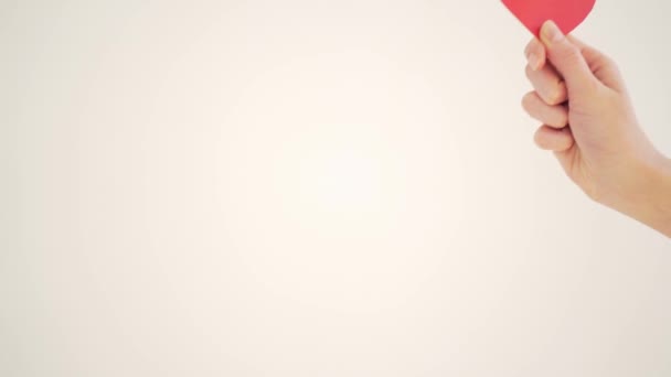 Rött papper valentin i en kvinnlig hand på en vit bakgrund. Alla hjärtans dag — Stockvideo