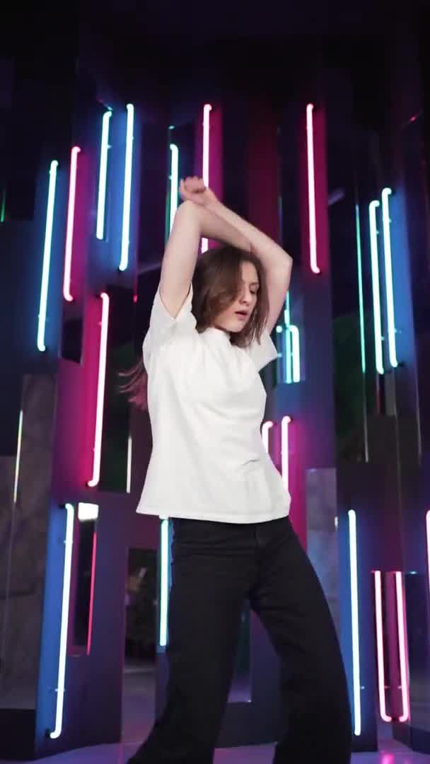 Vertical video - Enjoying the dance. Beautiful stylish woman having fun and dancing in a neon room — Stock Video