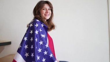 4k 10 bit. Bayraklı güzel bir Amerikalı kadın merdivenlerde oturur ve kameraya gülümser. ABD Ulusal Bayrağı