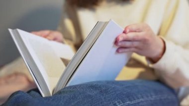 4K 10 bit. Genç bir kadın kitabı açıyor. Bilgi öğreniyorum. Ayaklarını yakın plan beyaz büyük kitap