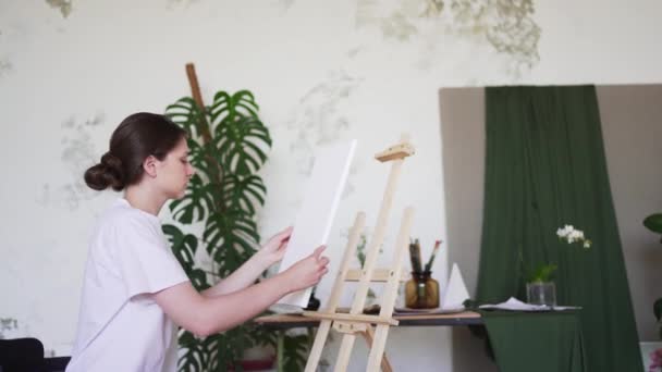 L'artista prepara un posto di lavoro in un laboratorio creativo. Pittore femminile installa tela bianca su cavalletto in legno — Video Stock