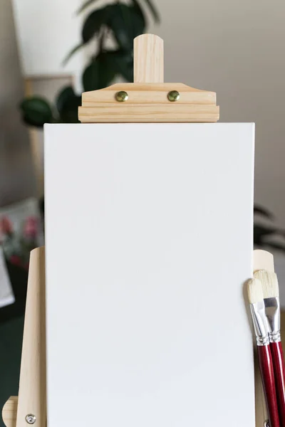 Kreatív stúdió. Üres fehér vászon egy fa festőállványon és vörös ecseteken — Stock Fotó