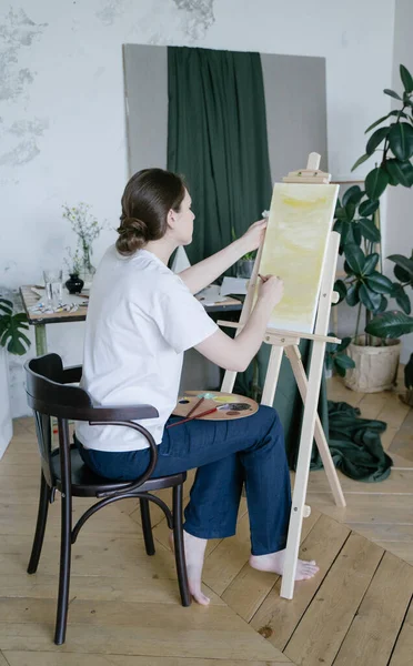 Creative entrepreneur. A young woman paints a picture in a spacious studio. Professional artist. Brushes and canvas on easel