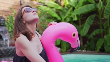 Flamingo 'daki havuzda güzel bir genç kadın. Pembe şişme yatak. Güneş gözlüğü. Yaz tatilinde eğlence.