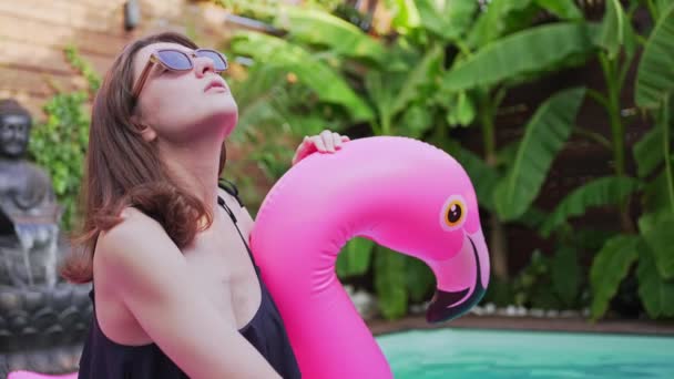Красива молода жінка в басейні на фламінго. Рожевий повітряний матрац. Сонцезахисні окуляри. Веселощі в літньому курорті на відпочинку — стокове відео