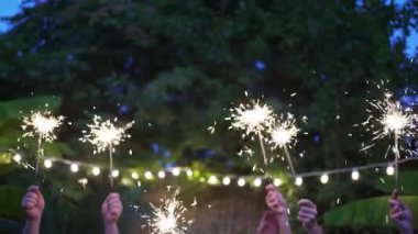 Bahçe partisi. Farklı insanların elleri maytapları tutuyor. Tropiklerde yeni yıl. Arkadaşlar dans ediyor ve eğleniyor.