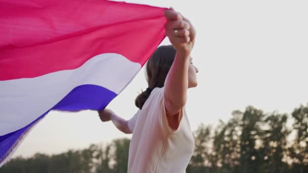 Dia da França. Uma mulher francesa com a bandeira nacional entra num campo ao pôr-do-sol — Vídeo de Stock