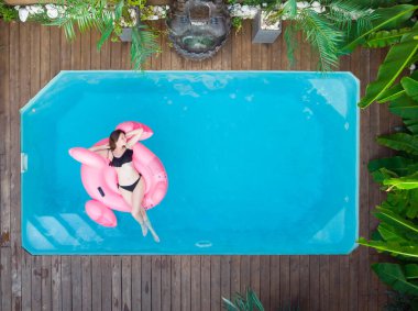 Havuzda pembe bir flamingoda yüzen bir kadın var. Hava manzaralı. Sudaki şiltenin üzerinde rahatla. Tatilde güneşlenen bayan.