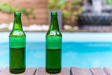 Dışarıda logosu olmayan iki yeşil bira şişesi. Tropiklerde yüzme havuzu. Bahçe partisinde alkol. Kimse yok.