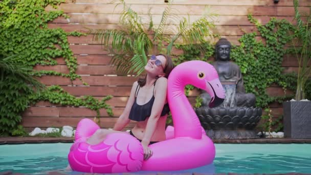 Молода жінка на рожевому матраці в басейні. Партія патіо, сонцезахисні окуляри — стокове відео
