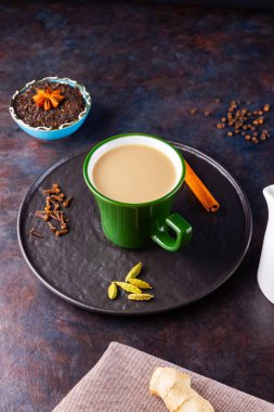 Masala çayı. Geleneksel Hint içeceği - siyah tabakta çeşitli baharatlar bulunan Masala çayı. Baharatlı seramik çay ve süt sürahisi