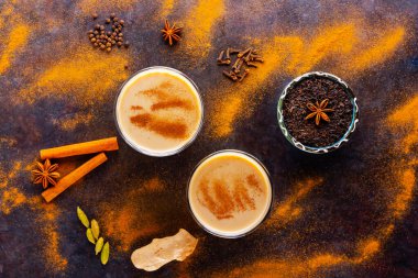 Siyah arka planda Masala çayı. İki şeffaf bardak Masala çayı ve çeşitli baharatlar. Üst görünüm