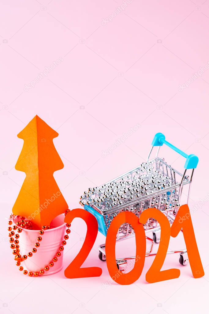 Red Christmas tree and the inscription 2021 in shopping cart. Christmas tree decorations in the shopping cart on a pink background. Holiday concept