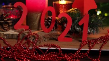Karanlık arka planda 2021 yılbaşı konsepti. Noel arkaplanda çelenk ışıkları var. 2021 yazıtında bir mum ve köy tarzı köknar dalları var. 4K